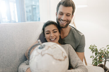 Glückliches Paar auf der Couch zu Hause mit Blick auf den Globus - MOEF00694