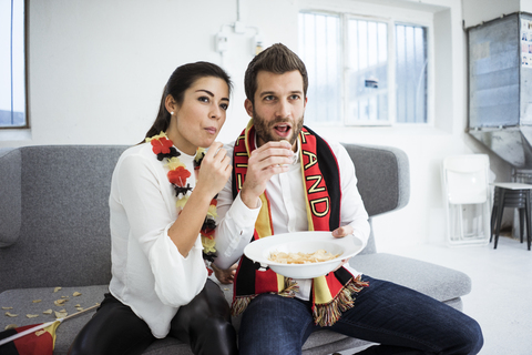 German football fan couple sitting on couch eating chips and watching Tv stock photo