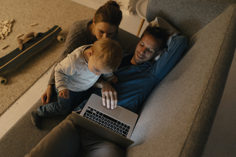 Familie benutzt Laptop auf der Couch im Dunkeln, lizenzfreies Stockfoto