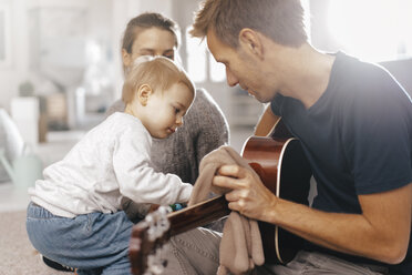 Little girl examining father's guitar at home - KNSF03407