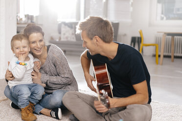 Glückliche Familie auf dem Boden sitzend, Vater spielt Gitarre - KNSF03408