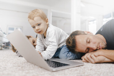 Parents sleeping with little girl using laptop on the floor - KNSF03411