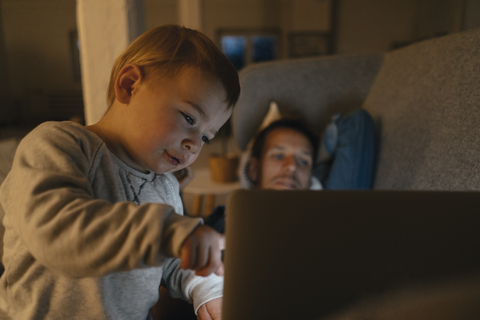 Litle girl with parents looking at laptop on the couch in the dark stock photo