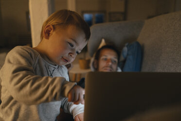 Kleines Mädchen mit Eltern, die auf der Couch im Dunkeln auf einen Laptop schauen - KNSF03413