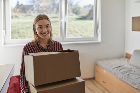 Portrait of smiling young woman carrying cardboard boxes stock photo