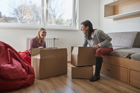 Zwei glückliche junge Frauen beim Auspacken von Kartons in einem Zimmer - ZEDF01077