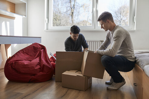 Zwei junge Männer packen Kartons in einem Zimmer aus - ZEDF01081