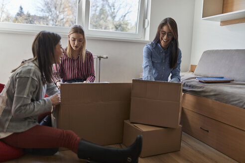 Drei glückliche junge Frauen beim Auspacken von Kartons in einem Zimmer - ZEDF01083