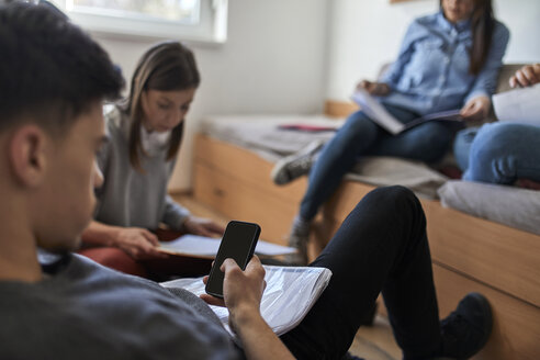 Studentin im Studentenwohnheim, die ihr Smartphone benutzt, mit Mitschülern im Hintergrund - ZEDF01088