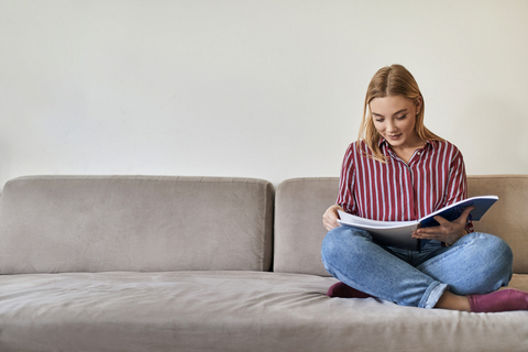 Young woman sitting on couch reading stock photo