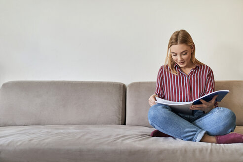 Junge Frau sitzt auf der Couch und liest - ZEDF01091