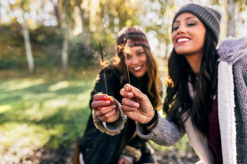 Zwei glückliche Frauen mit Wunderkerzen in einem herbstlichen Wald - MGOF03702