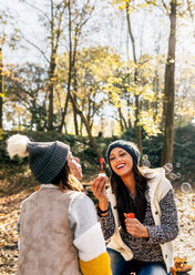 Zwei hübsche Frauen haben Spaß mit Seifenblasen in einem herbstlichen Wald - MGOF03705