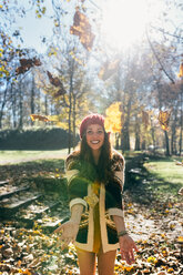 Portrait of a beautiful happy woman having fun with leaves in an autumnal forest - MGOF03710