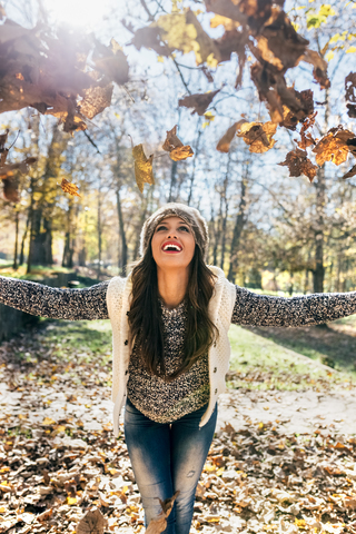 Schöne glückliche Frau hat Spaß mit Blättern in einem herbstlichen Wald, lizenzfreies Stockfoto