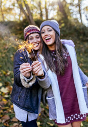 Zwei glückliche Frauen mit Wunderkerzen in einem herbstlichen Wald - MGOF03730