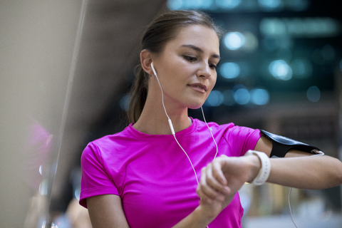 Young woman in pink sportshirt listening to music and checking her smartwatch stock photo