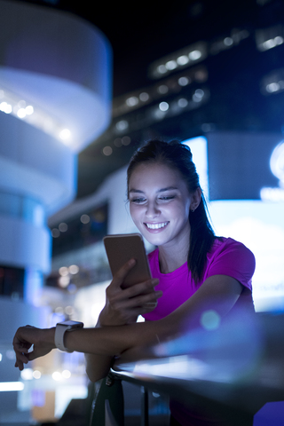 Junge Frau in rosa Sporthemd überprüft ihr Smartphone in der Stadt bei Nacht, lizenzfreies Stockfoto