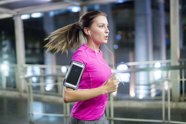 Young woman in pink sportshirt running in city at night - SBOF01003
