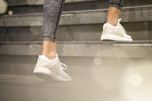 Close up of female legs with white sport sneakers running up the stairs - SBOF01006