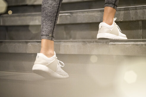 Nahaufnahme von weiblichen Beinen mit weißen Sportschuhen, die die Treppe hinauflaufen - SBOF01006