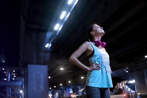 Young woman with pink headphones in modern urban setting at night stock photo