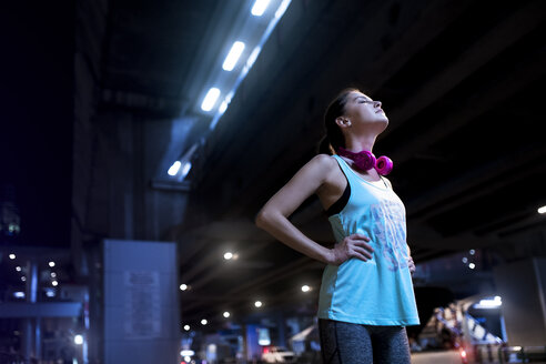 Junge Frau mit rosa Kopfhörern in moderner städtischer Umgebung bei Nacht - SBOF01009