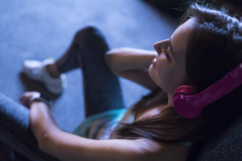 Glückliche junge Frau mit rosafarbenen Kopfhörern, die nachts in einer modernen städtischen Umgebung Musik hört - SBOF01022