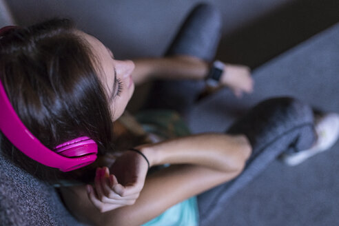 Happy young woman with pink headphones listening to music in modern urban setting at night - SBOF01023