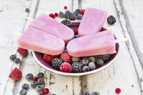 Hausgemachte Wildbeeren-Eislutscher mit Himbeeren, Heidelbeeren, Johannisbeeren und Brombeeren in einer Schale, lizenzfreies Stockfoto