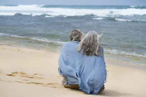 Älteres Paar am Strand sitzend, in eine Decke eingewickelt, lizenzfreies Stockfoto