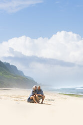 Senior couple sitting on the beach, wrapped in a blanket - SBOF01084