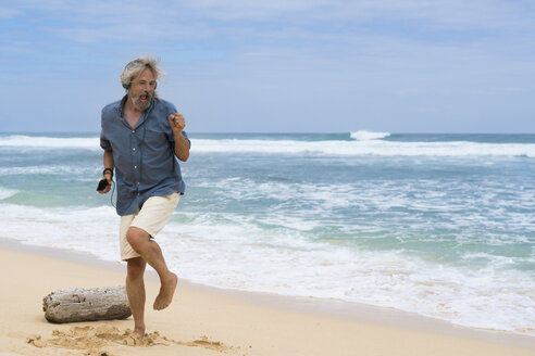 Handsome senior man with headphones dancing on the beach - SBOF01091