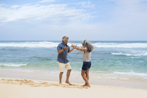 Hübsches älteres Paar mit Kopfhörern tanzt am Strand, lizenzfreies Stockfoto