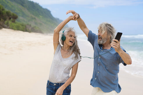 Hübsches älteres Paar mit Kopfhörern tanzt am Strand - SBOF01095
