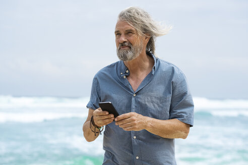 Hübscher älterer Mann mit Smartphone am Strand - SBOF01106