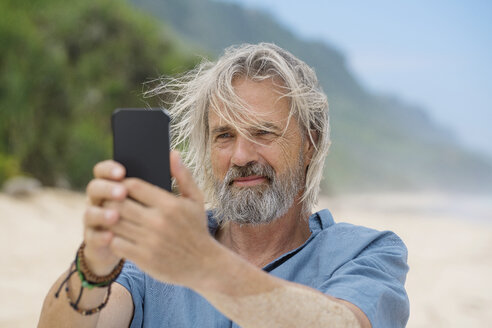 Gutaussehender älterer Mann, der ein Foto mit seinem Smartphone am Strand macht - SBOF01107