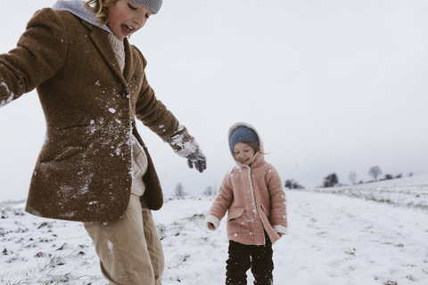 Bruder und kleine Schwester spielen zusammen auf einer schneebedeckten Wiese, lizenzfreies Stockfoto