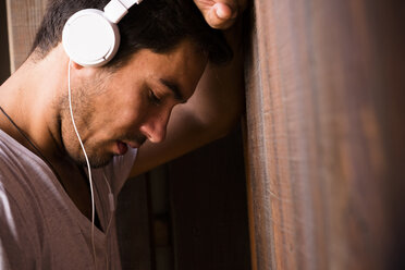 Serious young man wearing headphones leaning against wooden wall - SIPF01918