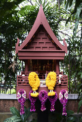 Thailand, Bangkok, Nachbildung eines Hauses im thailändischen Stil als kleine, mit Blumen geschmückte buddhistische Kapelle - IGGF00374