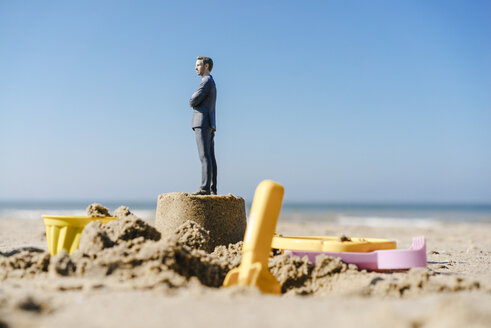 Businessman figurine standing on sand with toys around - FLAF00003