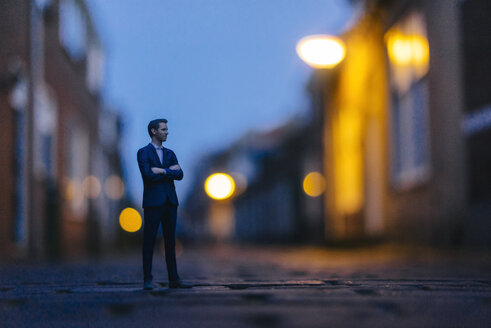 Businessman figurine standing in street in front of houses - FLAF00007