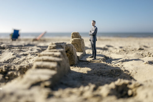 Businessman figurine standing on sand by sand buildings - FLAF00010