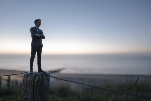 Businessman figurine standing on a fence at the beach, looking at the sea - FLAF00011
