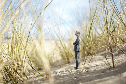 Businessman figurine standing on sand dune, looking at distance stock photo