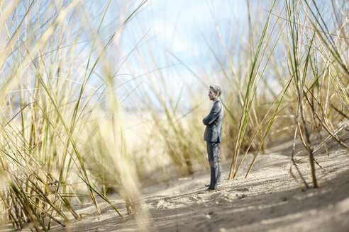 Businessman figurine standing on sand dune, looking at distance - FLAF00016