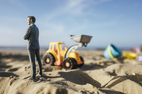 Businessman figurine standing on sand with toy digger, investment in home ownership stock photo
