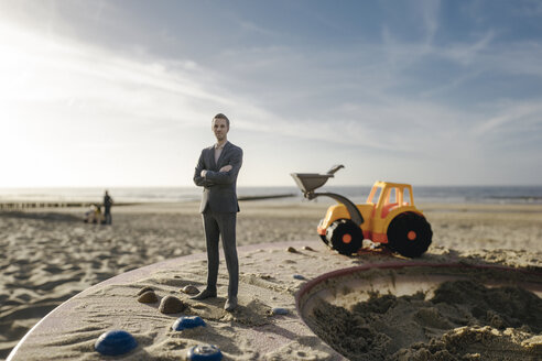 Businessman figurine standing on sand with toy digger, investment in home ownership - FLAF00021