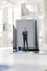 Businessman figurine standing on portable devices in a glass cage - FLAF00026