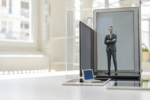 Businessman figurine standing on portable devices in a glass cage - FLAF00027